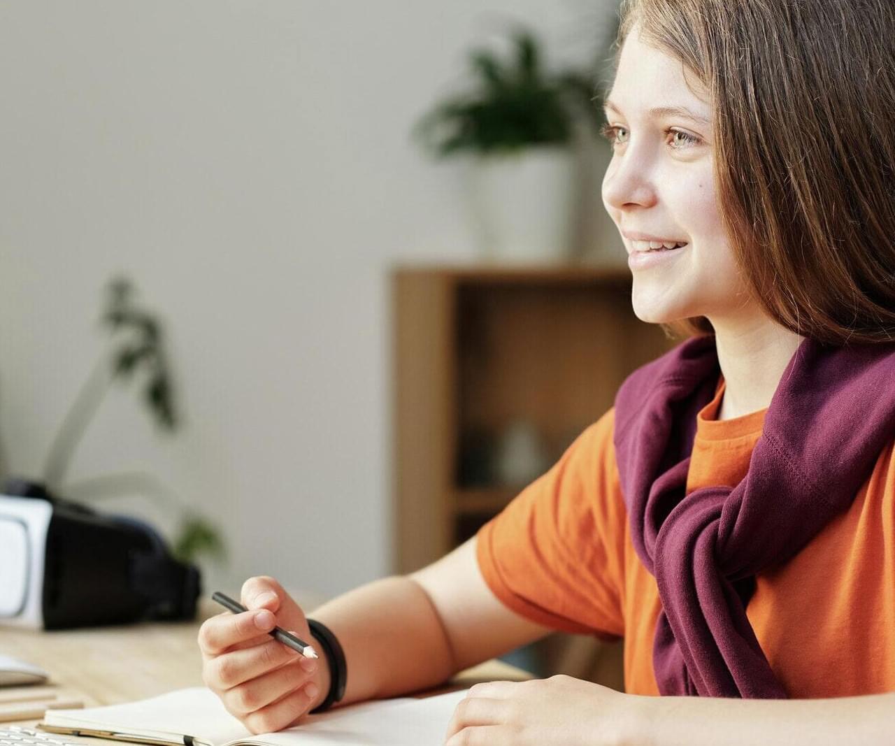 a young girl sitting with a pen and pad, smiling